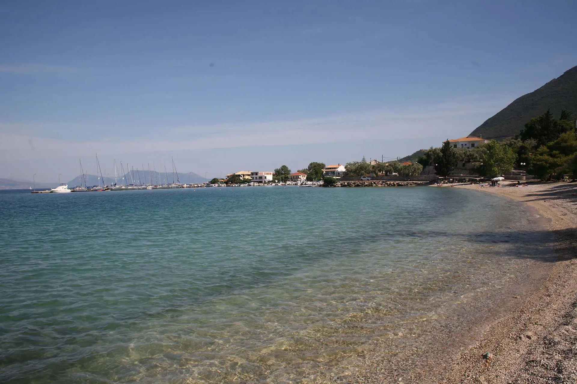 Τα ήρεμα, καθαρά νερά και η βοτσαλωτή ακτή της παραλίας της Λυγιάς, με ψαροκάικα στο γραφικό λιμάνι.