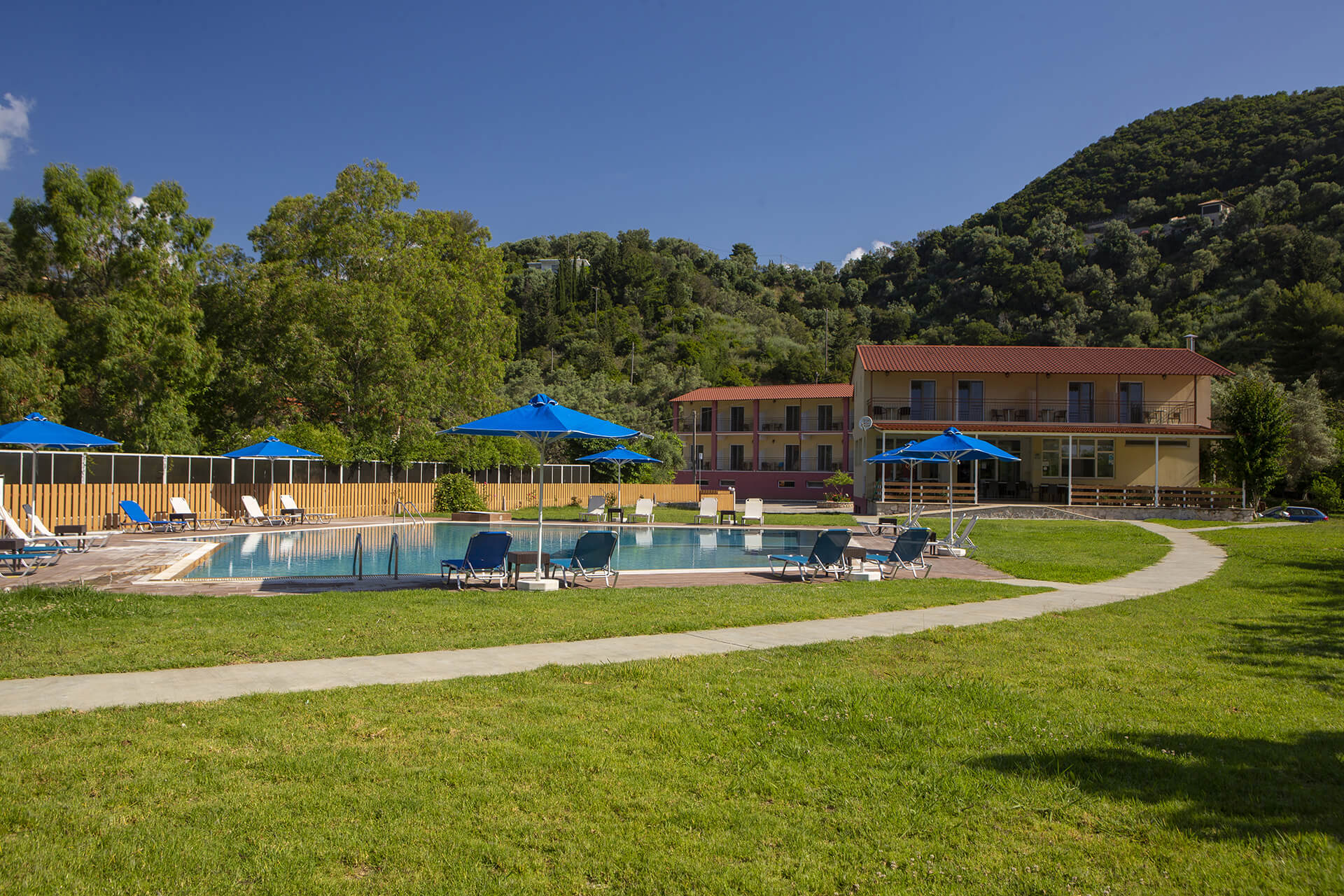 Tents and caravans nestled under olive trees at Santa Maura Camping, with the sea of Desimi bay visible.