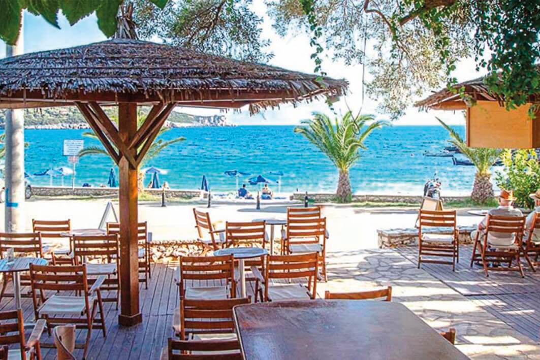 Το εκπληκτικό παραθαλάσσιο σκηνικό του Ammousa Beach Café & Restaurant, με τραπέζια και ξαπλώστρες δίπλα στα καθαρά τυρκουάζ νερά.