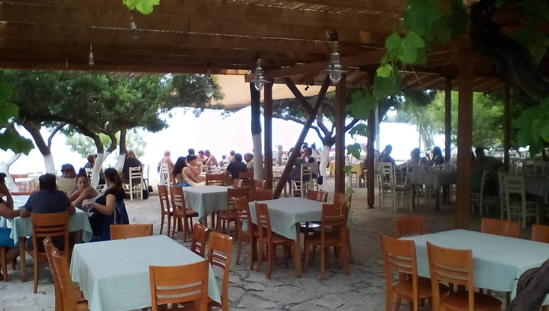 Το όμορφο παραθαλάσσιο σκηνικό του Breath of Zorbas στη Νικιάνα, με τραπέζια εστιατορίου και ξαπλώστρες στην παραλία.
